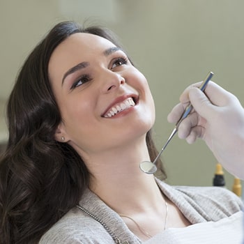 A smiling woman in the dentist's chair with a dental mirror