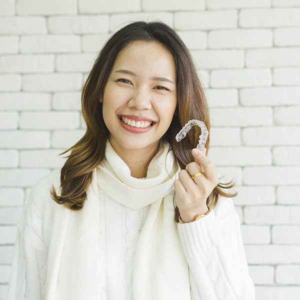 A teenage woman holding invisalign aligners while smiling